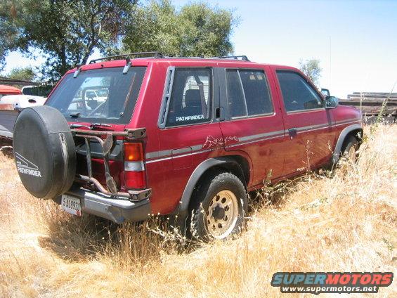 Red SUV with spare tire mounted on rear carrier, parked in dry grass. 'PATHFINDER' text visible
