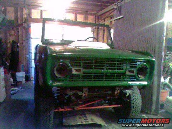 Green 1974 Ford Bronco front end, missing headlights, in a garage
