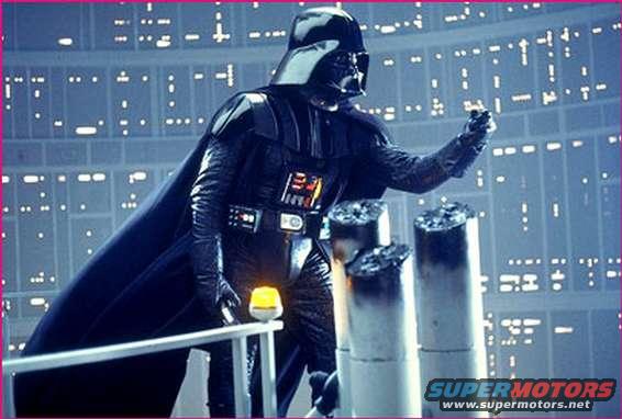 Darth Vader in a dark costume stands on a platform with metallic structures and a glowing yellow light