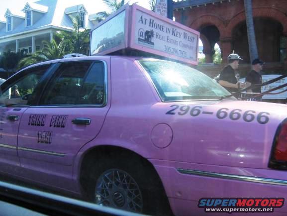 Pink taxi with 'THINK PINK TAXI' on the side and phone number 296-6666. Sign on top says 'AT HOME IN KEY WEST REAL ESTATE COMPANY'