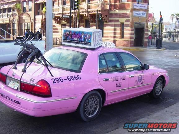 Pink taxi cab with a bike rack on the trunk, parked on a street