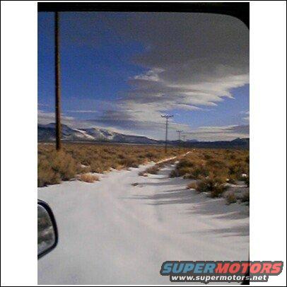 view down a snowy road with scrub brush and utility poles under a cloudy sky