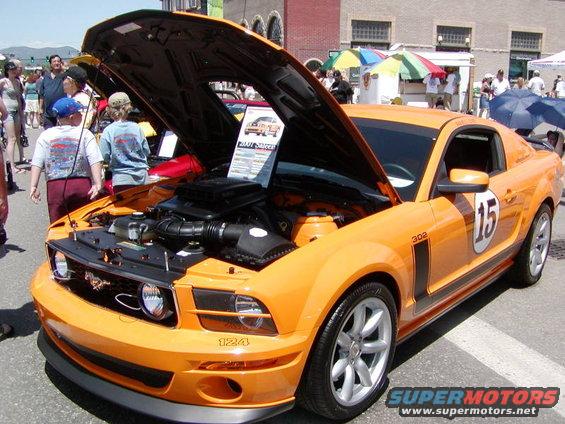 Orange Saleen Mustang with hood open, showing engine and a display board. Number 15 on door