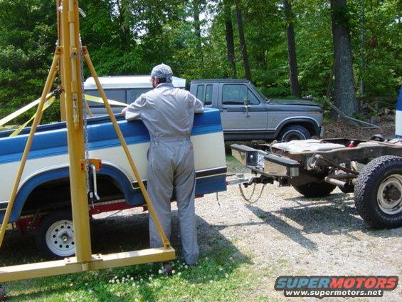 Two-tone Ford F-Series truck bed lifted by yellow engine hoist, with a gray Ford F-Series pickup in the background