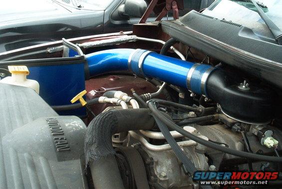 Engine bay with blue intake tube, air filter housing, and radiator fan shroud. Maroon vehicle