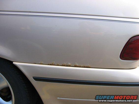 Close-up of a car's rear quarter panel showing rust along the lower trim line