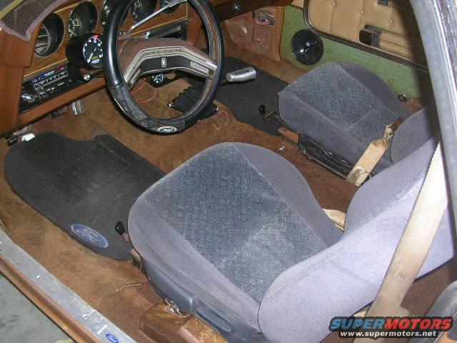 Interior view of car with bucket seats, steering wheel, and floor mats with Ford logos