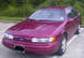 1995 Ford Taurus - Maroon 1995 Ford Taurus sedan parked in a lot with trees in the background.