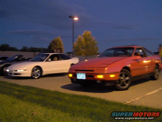 Red coupe in foreground, white coupe behind it. Dusk lighting