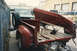 1967 Ford F-100 - A red pickup truck bed is shown with its tailgate open, revealing wooden planks and a spare tire. Another truck is visible in the backgroun…