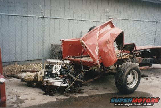 Wrecked red pickup truck chassis with engine and transmission removed, sitting outside