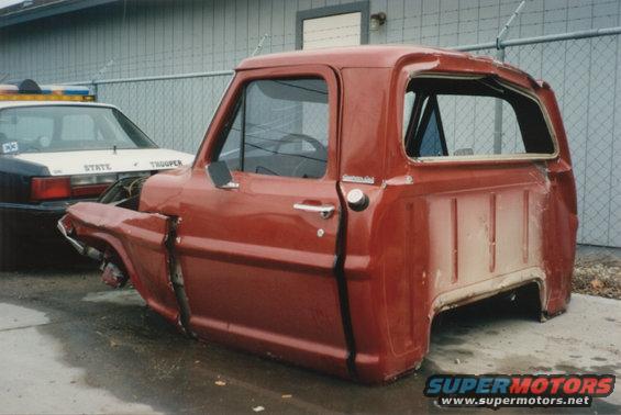 Red 1967 Ford F-100 truck cab and front clip, damaged, parked next to a state trooper car