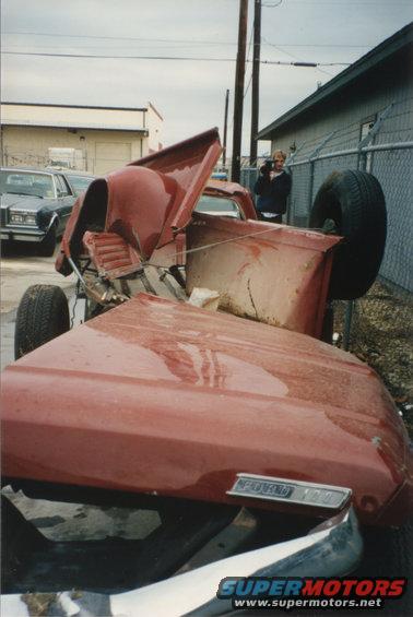 Red 1967 Ford F-100 pickup truck, heavily damaged and overturned, with hood open and front end crushed