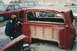 1967 Ford F-100 - A person photographs a damaged red 1967 Ford F-100 pickup truck cab in a junkyard setting.