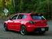 2007 Mazda 3 - Red Mazda 3 hatchback with aftermarket wheels and spoiler parked on a gravel road.