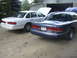 1997 Ford Crown Victoria - Two Ford Crown Victorias, a white and a blue model, are parked in front of a garage with their hoods open.