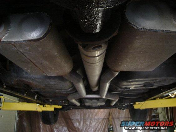 Underside view of a car's exhaust system and driveshaft, with a yellow lift pad visible
