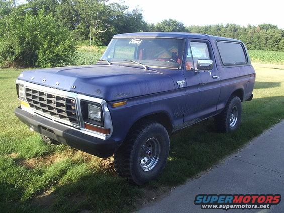 Blue 1978 Ford Bronco parked on grass next to a paved surface