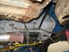 1973 Ford Ranchero - The photo shows the underside of a vehicle, focusing on the transmission and exhaust system, with a chain supporting some of the components.