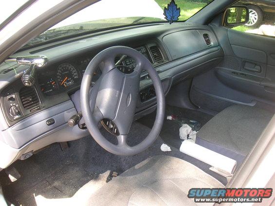 Car interior shot showing dashboard, steering wheel, and seats. A blue air freshener hangs from the rearview mirror