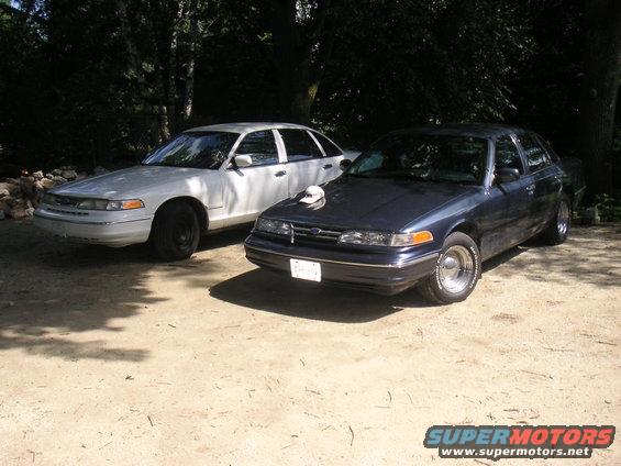 Two 1997 Ford Crown Victorias parked outdoors, one white and one dark blue