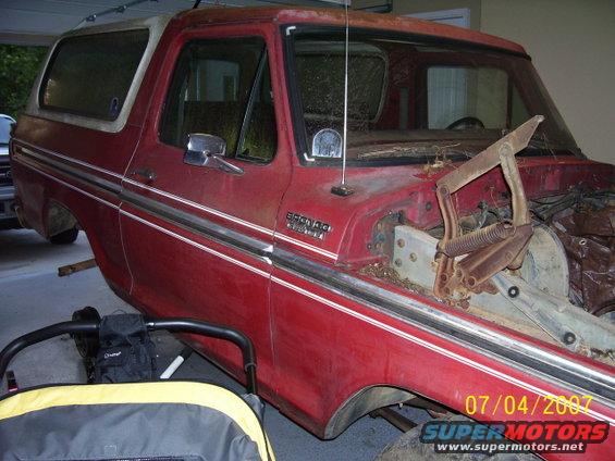 Red 1979 Ford Bronco with white trim, hood removed, in a garage