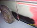 1979 Ford Bronco - Close-up of a vehicle's damaged side panel and fender, showing rust and primer, with a flat tire visible.