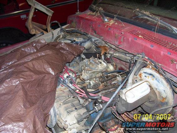 Engine bay with a tarp covering part of the engine. Red vehicle body visible
