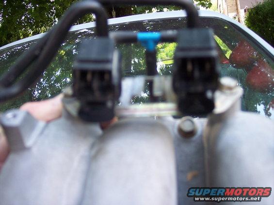 Close-up of fuel injectors attached to an intake manifold, with a hand holding the part
