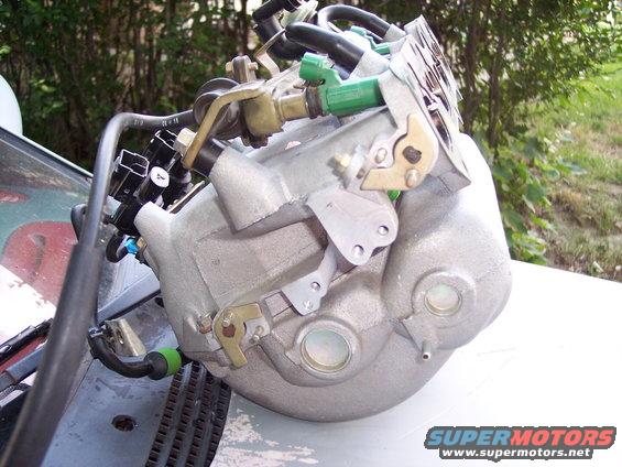 Aluminum intake manifold with green fuel injectors and black hoses attached