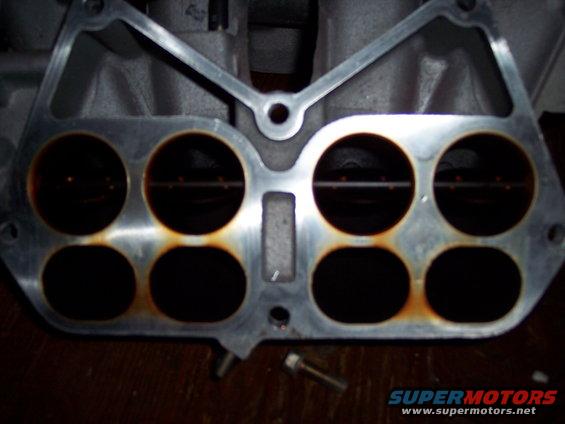 Close-up of an engine intake manifold with eight ports, showing rust around the edges