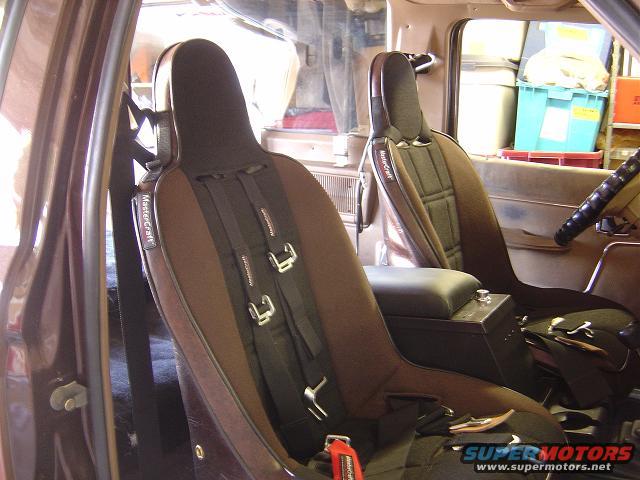 Brown racing seats with MasterCraft harnesses inside a vehicle, viewed from the passenger side door