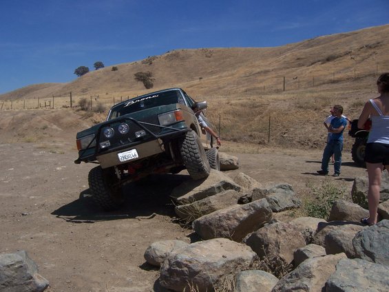 Green Ford Bronco driving over rocks on a dry, grassy hill. License plate reads 2REU146