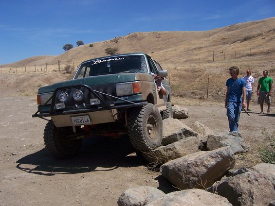 Green and tan 1991 Ford Bronco off-roading over rocks