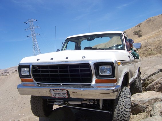 White Ford truck with a black grille and chrome bumper, driving over rocks