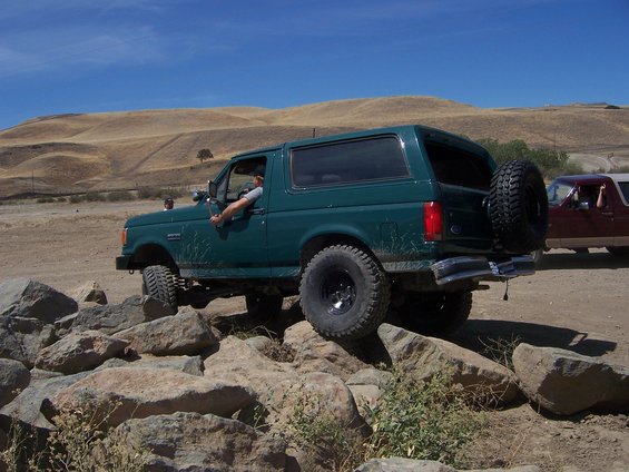 Green 1991 Ford Bronco navigating rocky terrain with another vehicle behind it