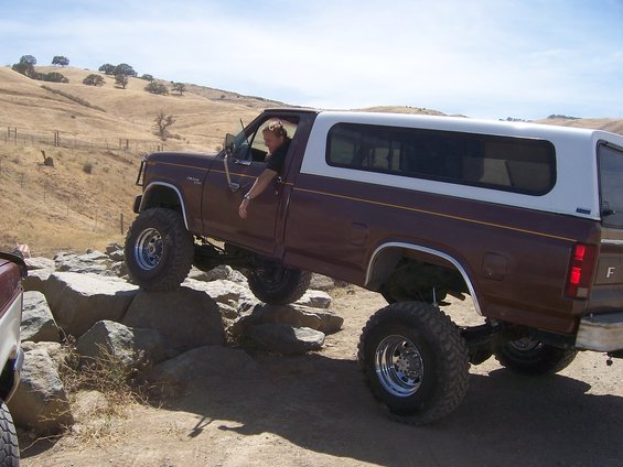 Brown Ford pickup with white camper shell driving over rocks. Driver is visible