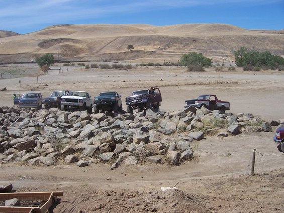 Several trucks and SUVs are parked on a rocky incline in a dry, hilly landscape