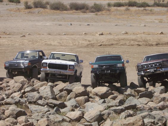 Four trucks on rocks, white truck has 1980s Ford F-Series styling