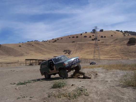 Green 1991 Ford Bronco climbing over a log on a dirt trail
