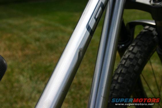 Close-up of a silver bicycle frame with a dent. Tire visible in background
