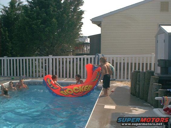 Kids playing on an inflatable 'Rocker' pool toy in a backyard pool