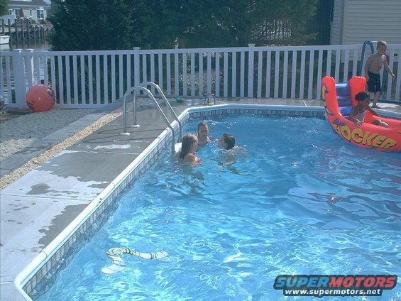 Children swim in a backyard pool with a white fence and an inflatable toy
