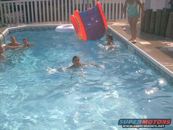 Children playing in a backyard swimming pool with an inflatable slide