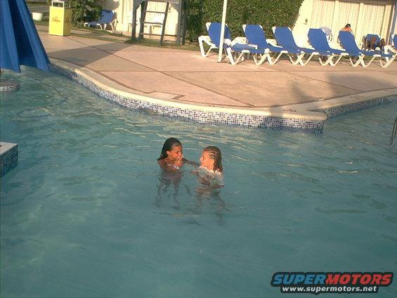 Two girls playing in a swimming pool with lounge chairs and a slide in the background