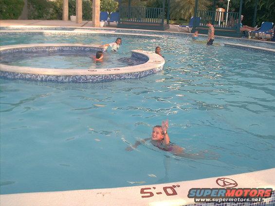 Pool with people swimming, depth markers on the edge, and a SuperMotors logo