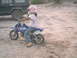 2003 Yamaha RAPTOR 80 - A person rides a blue dirt bike on a sandy track next to a black SUV.