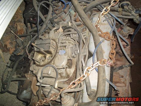 Engine block with carburetor, distributor, wiring, and a rusty chain. Watermark reads www.supermotors.net