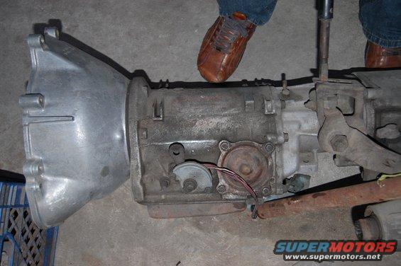 automatic transmission with wires and linkage visible, person's shoes in background