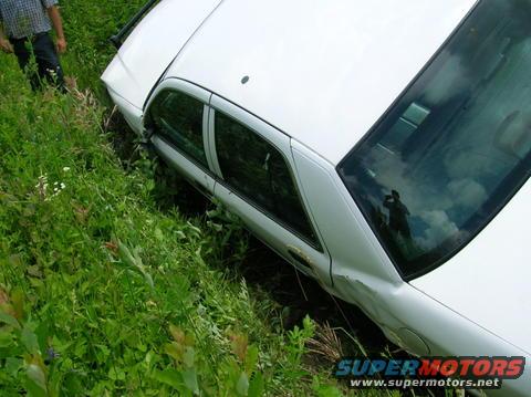White 2003 Ford Crown Victoria in a ditch, side view, dented rear quarter panel